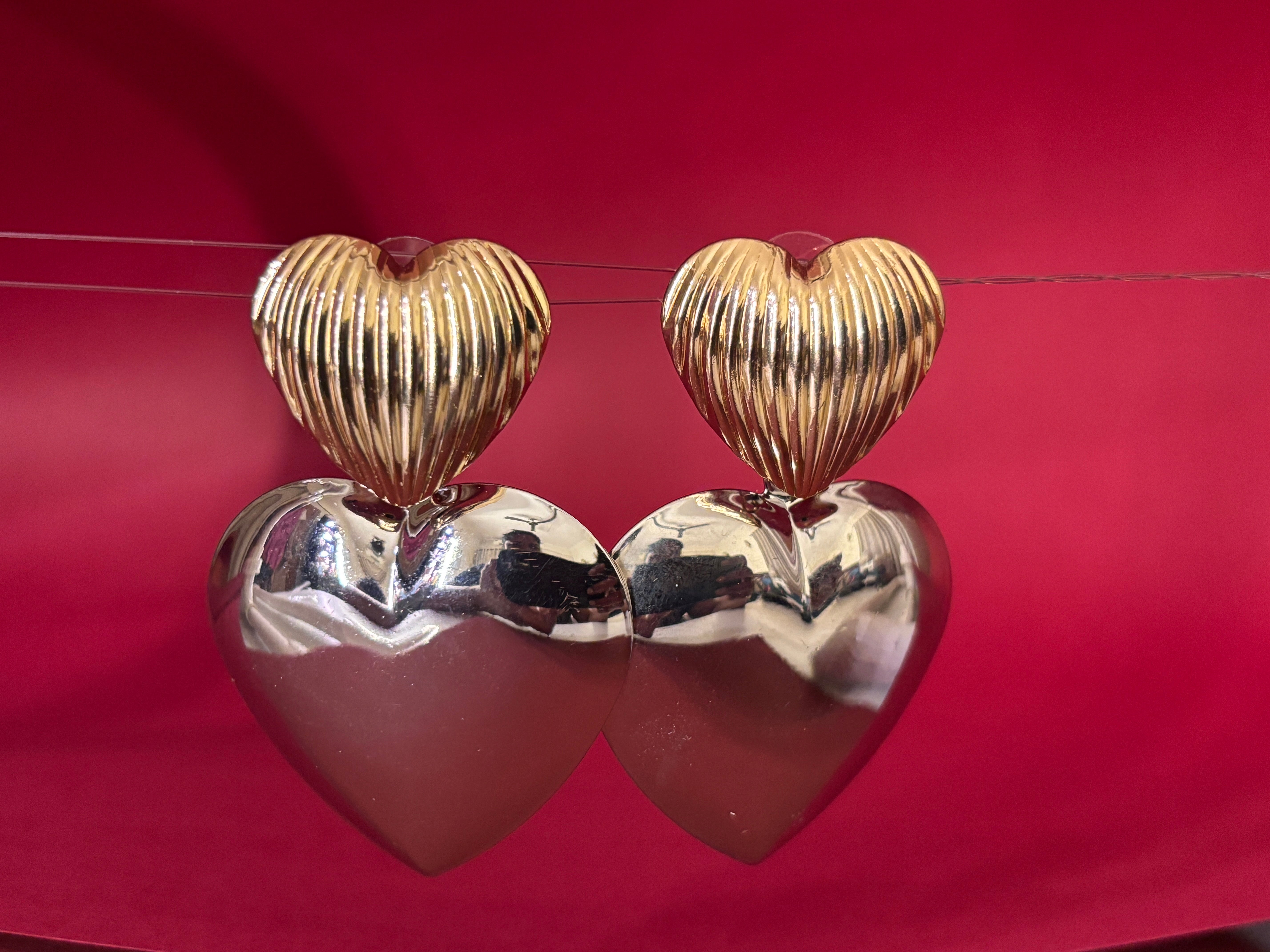 Heart-shaped earrings in gold and silver on a red background